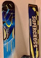 Close-up of the ski with blue, black, yellow graphics and 'Supercross' branding on one ski.