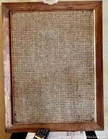 Front view of one wall speaker showing wood frame and woven fabric grill