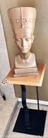 Full view of Nefertiti bust statue on the square wooden top table with black twisted iron base.