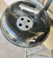 Top view of the black Weber grill lid showing vent and white handle, with some paint wear.