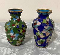 Front view of two mini Chinese cloisonné vases, one primarily green and the other blue, showing detailed floral enamel work and gold wire outlines.