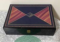 Closed rectangular wooden case with high gloss finish, diamond pattern in mahogany and black colors, brass latch on front.