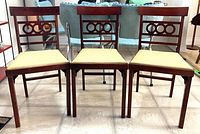 Front view of three wooden folding chairs with yellow padded seats and decorative backed design