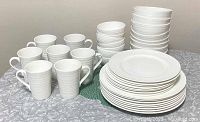 Full display group of 38 pieces showing dinner plates, salad plates, bowls, and mugs arranged on a textured surface to show size and quantity of collection.
