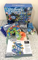 Opened box of Discovery Mindblown Marble Run with colorful plastic pieces mostly sealed in original bags, including various track segments, gears, connectors, and instructions.