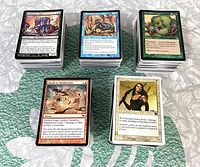 Five stacks of assorted Magic The Gathering cards showing card faces including Deathcurse Ogre, Smash to Smithereens, and Avacynian Archers.