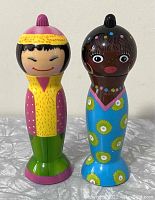 Front view of two colorful figurine-style salt and pepper mills on white surface with beige background.