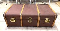 Closed reddish brown steamer trunk with bentwood trim and metal locks in front, placed on tiled floor.