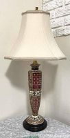 Side view of lamp showing ceramic base with red and white geometric patterns and cream bell shade with gray trim.