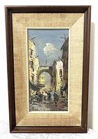 Full view of framed oil painting showing a vertical street scene with crowd, archway, and buildings, with a linen mat and dark wooden frame with wear.