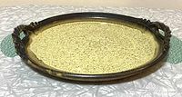 Top and angled view of a round pottery tray with speckled yellow glaze and brown tinted edges with sculpted handles.