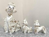 Front and side view of the three white porcelain poodles with spaghetti style textured fur and gold highlights.