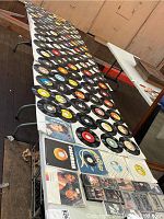 Two long tables covered with a large number of vinyl 45 RPM records arranged in rows, along with a few audio cassette tapes grouped in plastic cases at one end.