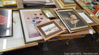 Collection of multiple framed art pieces and prints laid out on a table, showing sizes, framing styles, and art themes including ballerina and landscape.