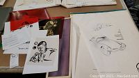 Mixed medium drawings and prints on a table, including a black and white portrait graphic and handwritten notes