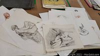 Stack of loose drawings and sketches on a table, mostly white paper with pencil and ink drawings showing human figures.