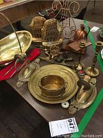 Full view of lot on table showing brass basket, brass cathedral bookends, oval wall sconces, candle holders, bell, cup and plate, copper pitcher, and duck hooks