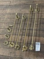 Four brass towel bars with decorative floral leaf base mounts arranged on wooden floor