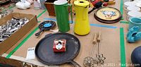 Overview of cast iron fry pan, green and yellow enamelware pitchers, mini enamelware plate, and two rosette wands on a table.