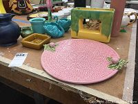 Overview of ceramic items including blue McCoy planter, pink cake plate with leaf handles, yellow-green tulip vase, teal Goebel swans, mustard square dish, and small green pitcher