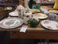Full view of the china items laid out on a wooden table showing various tea pots, plates, mugs, and glass.