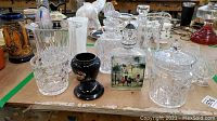 Overview of crystal decanters, lidded jar, small black pedestal holder, and other glass items arranged on a tabletop