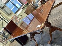 Full view of the wood dining table with one leaf partially extended, showing polished surface and claw foot legs.