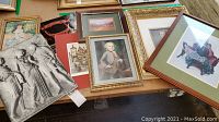 Overview photo showing several framed prints and posters on a table, varying in size and subject matter including portraits and architectural imagery.