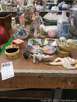 Multiple porcelain and ceramic decorative items including figurines, small boxes, and vases, laid out on a table for inspection.