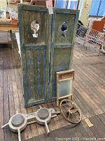 Front view of distressed wooden shutters with washboard, wheel, and wooden decor on floor