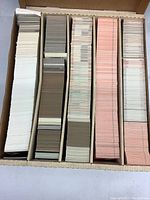 Top-down photo showing five rows of trading cards in a cardboard box separated by dividers in various colors such as white, brown, and peach.