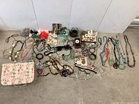 Wide view of the entire costume jewelry lot showing numerous bracelets, necklaces, rings, earrings, a wristwatch, sunglasses, a large red flower hair accessory, and a floral fabric pouch.