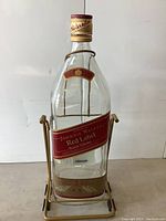 Front view of giant Johnnie Walker Red Label empty glass bottle in metal stand with pump.