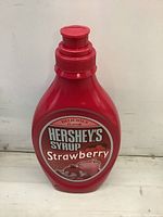 Front view of red plastic piggy bank shaped like a Hershey's Strawberry Syrup bottle with label