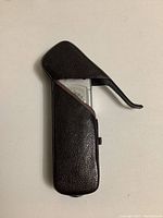 Minox spy camera partially inserted in black leather fitted case with flap open, showing side profile