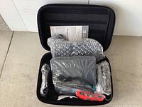 Carrying case open showing dock, console, Joy-Con controllers, straps, cables, grip, and manual