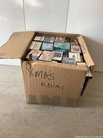 Wide shot of a large cardboard box labeled 'XMAS ALBUMS' filled with cassette tapes.
