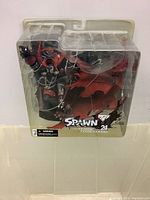 Front angled view of sealed Spawn action figure with visible packaging branding and detailed figure inside with red cape wings.