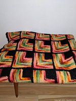 Folded afghan blanket showing colorful squares with gradient color pattern in pink, yellow, green, orange and black