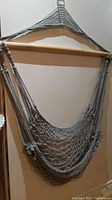 Full view of a gray woven hanging hammock chair with a wooden support bar and suspension rope attached to the top for hanging.