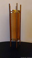 Full view of mid century table lamp showing cylindrical weave shade, teak wood legs, and metal accents
