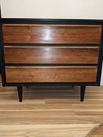 Front view of dresser showing three walnut drawers with matte black frame and tapered legs.