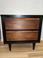Front view of vintage night stand showing matte black frame and two walnut drawers