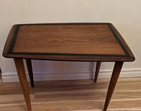 Front angle view of trapezoid teak side table, showing wood grain and tapered legs.