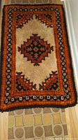Full view of the vintage latch hook rug showing the overall geometric and floral pattern with gold, orange, brown, and cream colors.