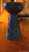 Front and side view of blue glazed ceramic candle holder showing conical base with circular decorations.
