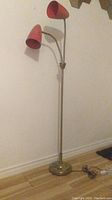Full view of the vintage double gooseneck floor lamp showing two red fiberglass shades and metal base.
