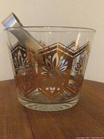 Front angled view of the clear glass ice bucket showing the gold floral geometric pattern with included metal tongs inside