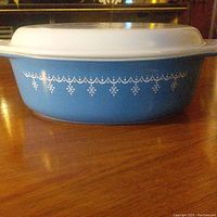 Side view of blue Pyrex casserole dish with white snowflake and garland pattern and fitted white lid