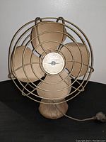 Front view of vintage Randi-Regal electric fan showing the four blades and logo on central hub, metal wire protective cage around blades, beige color showing wear.